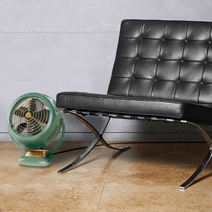 Green vintage-style fan next to a black leather chair on a wooden floor.