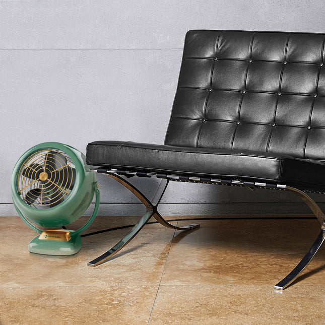 Green vintage-style fan next to a black leather chair on a wooden floor.