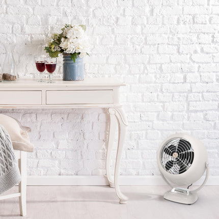 Vintage-style fan on a white surface with a decorative table and white brick wall in the background.