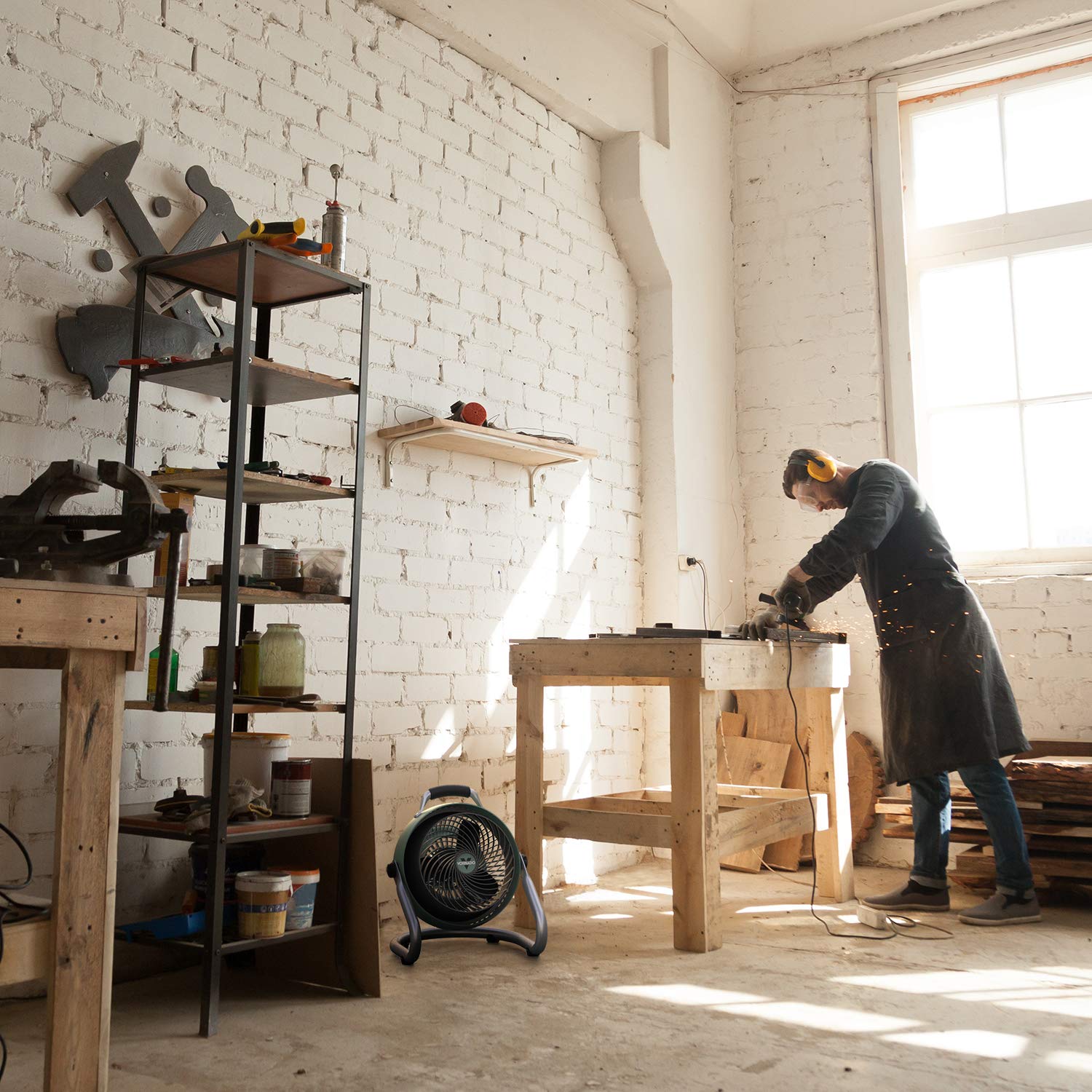 Person working in a workshop with tools and equipment on shelves using a Vornado fan