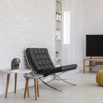 Modern living room with a black lounge chair, white brick wall, and wooden furniture. A gray portable fan is present on a white end table