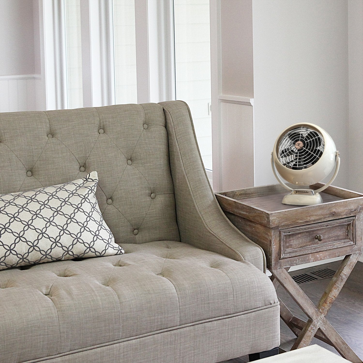 Beige tufted sofa with a decorative pillow next to a wooden side table with a vintage-style fan.