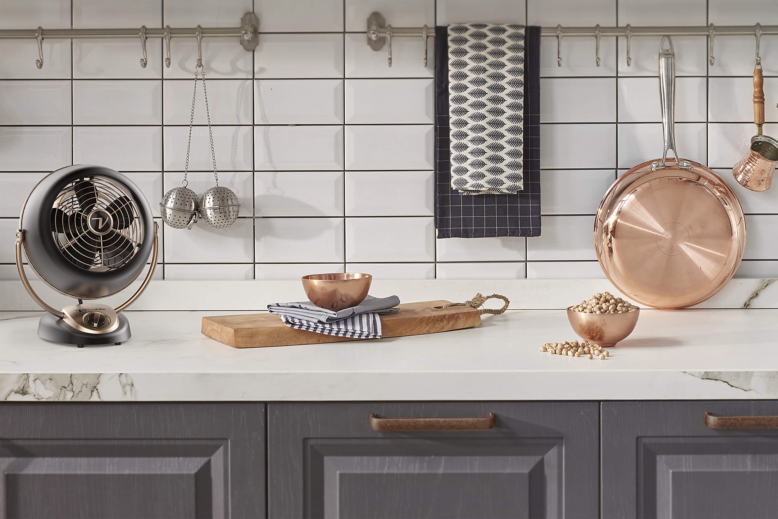 Modern kitchen with copper pots, wooden cutting board, and decorative items on a white countertop.