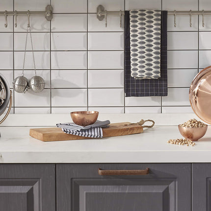 Modern kitchen with copper pots, wooden cutting board, and decorative items on a white countertop.