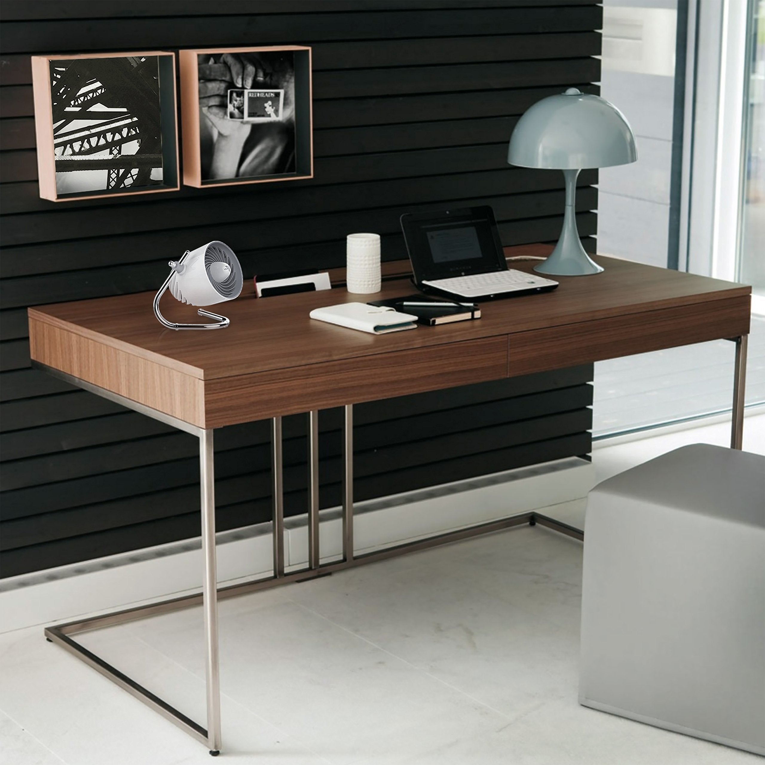 Modern office desk with laptop, lamp, and fan in a stylish room.