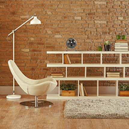 Modern living room with a white chair, floor lamp, and vintage fan on a bookshelf