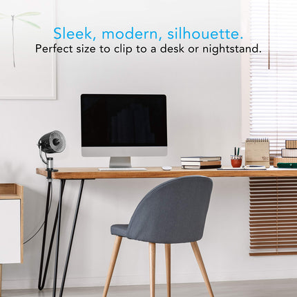 Modern office desk with computer monitor, chair, and decor items against a white wall. A clip fan is present on the end of the table