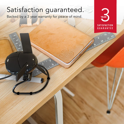 Black fan on a desk with a brown leather notebook, ruler, and orange chair. Text 'Satisfaction guaranteed' and '3 Year Satisfaction Guarantee' displayed.