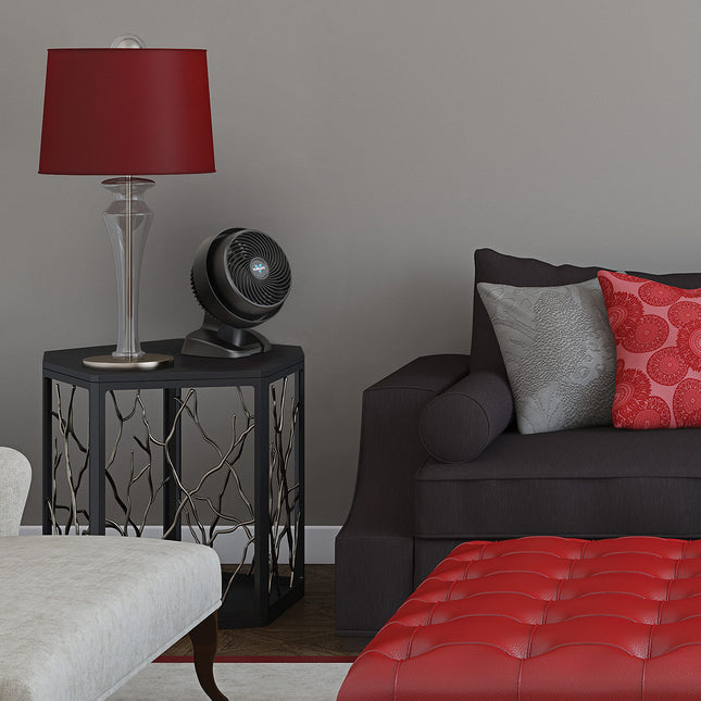 Living room with a dark gray sofa, red ottoman, and a fan on a side table.