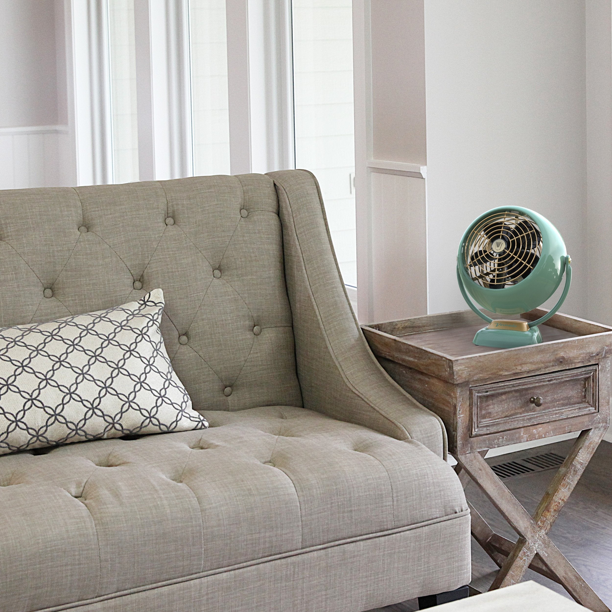 Beige tufted sofa with a decorative pillow and wooden side table with a vintage-style fan.