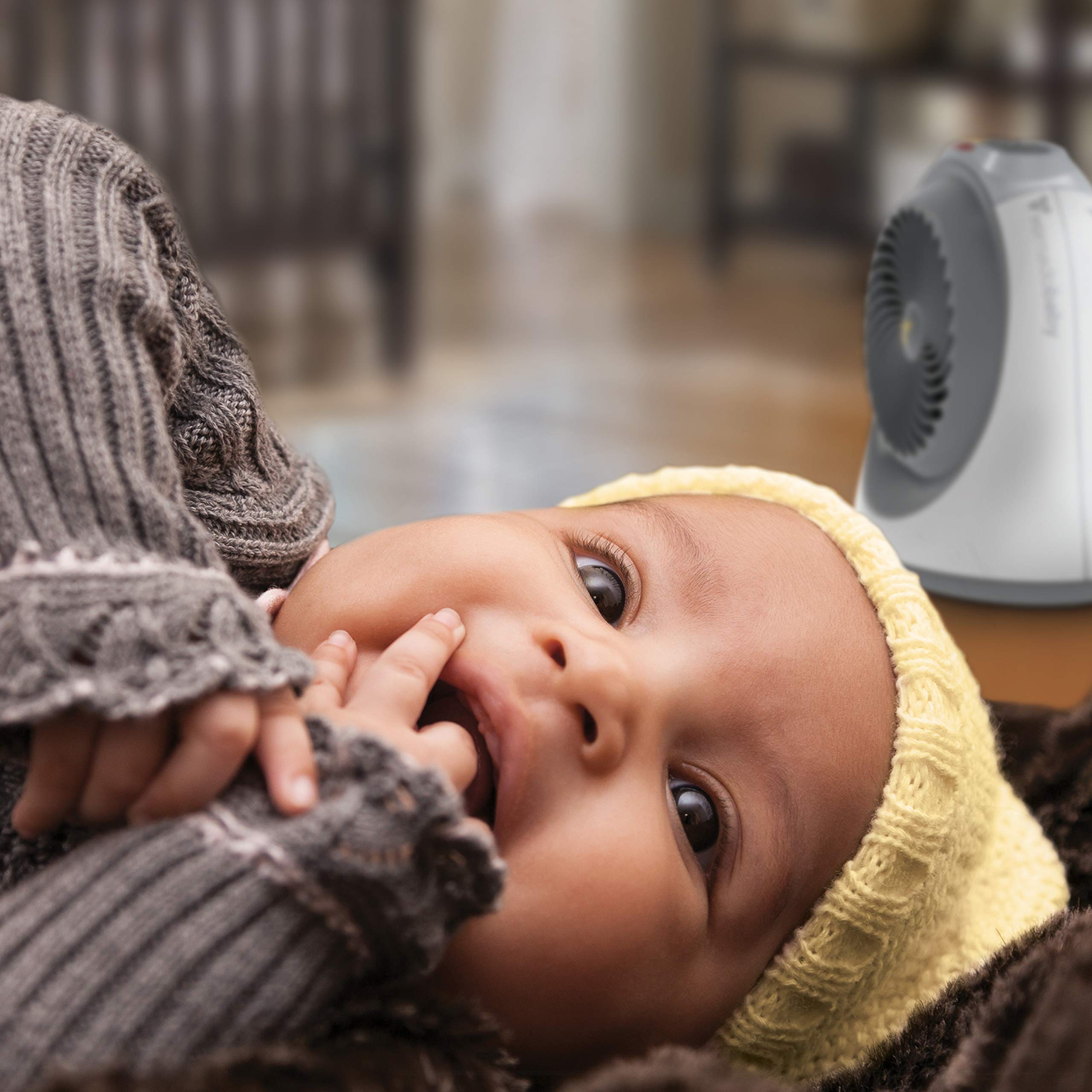 Baby wearing a yellow headband and gray sweater with a heater in the background