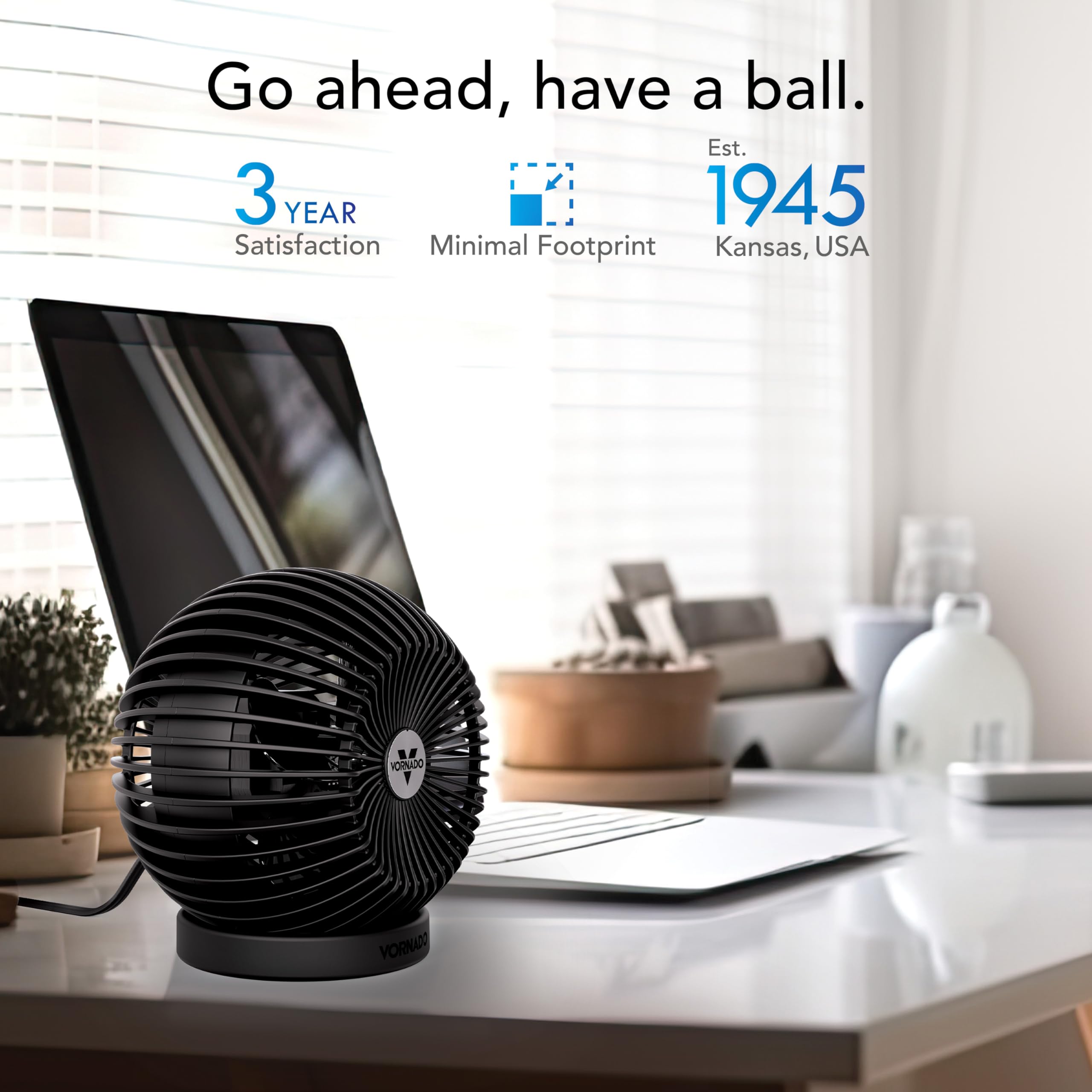 Black desk fan on a desk with a laptop, minimal footprint highlighted text, and a blurred living room background.