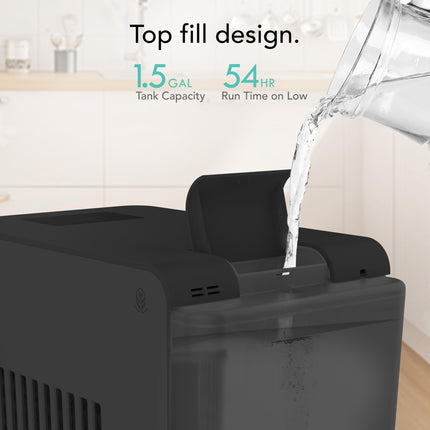 Black water dispenser with top fill design, showing water being poured in, on a kitchen counter.