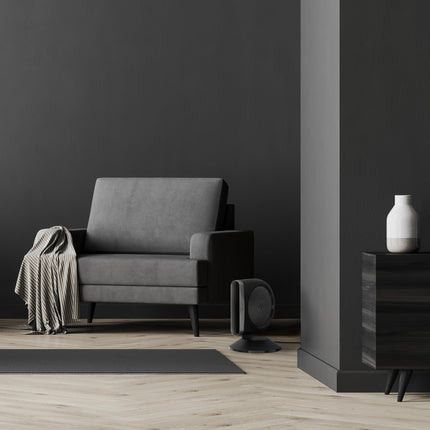 Gray armchair in a minimalistic room with a blower fan and wooden floor.