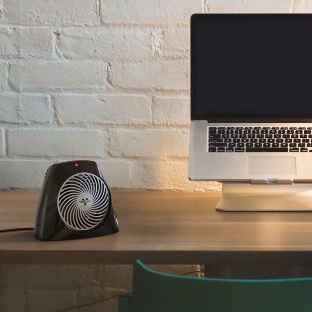 Small black fan on a desk next to a laptop with a white brick wall background