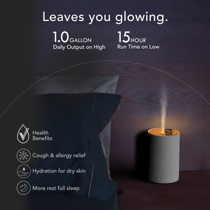Diffuser emitting mist next to a pillow with health benefits listed on a dark background