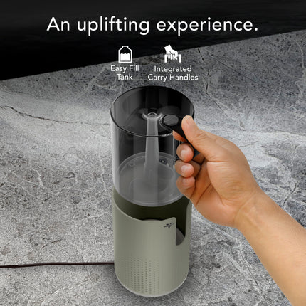 Hand holding a humidifier tank with text highlighting features on a gray surface