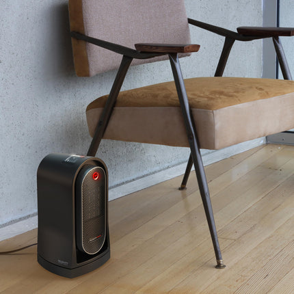Portable ceramic heater on a wooden floor with a chair in the background