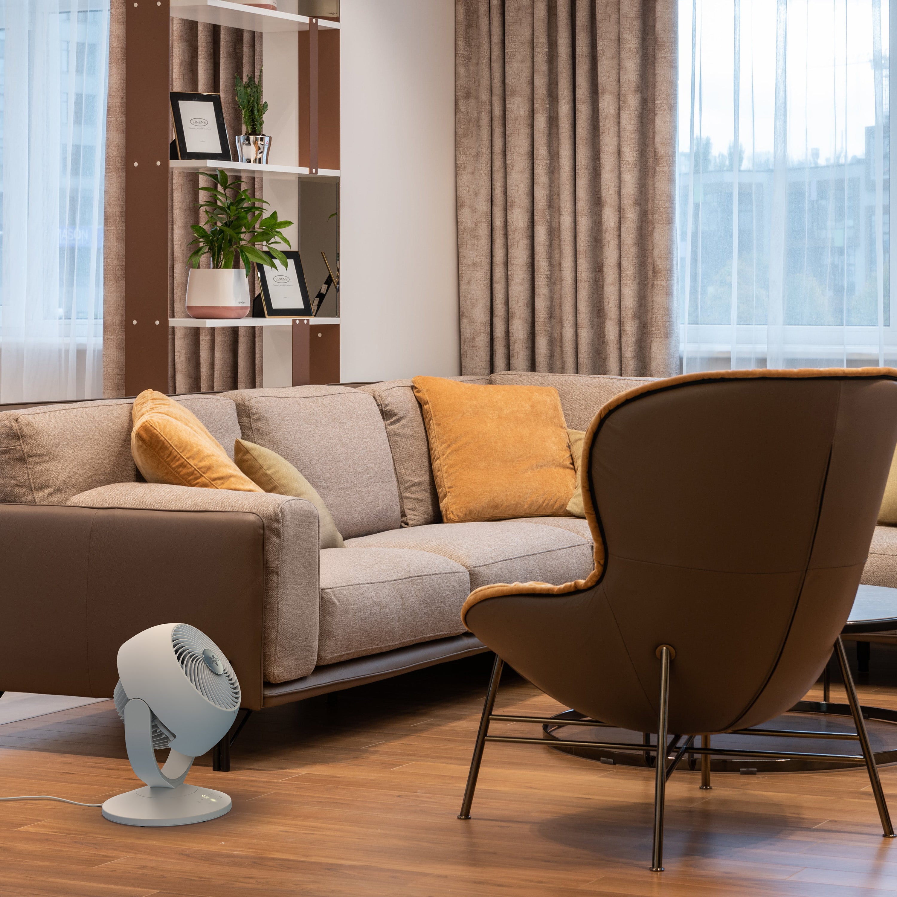 Modern living room with a gray sofa, brown chair, and a small white fan on the floor.