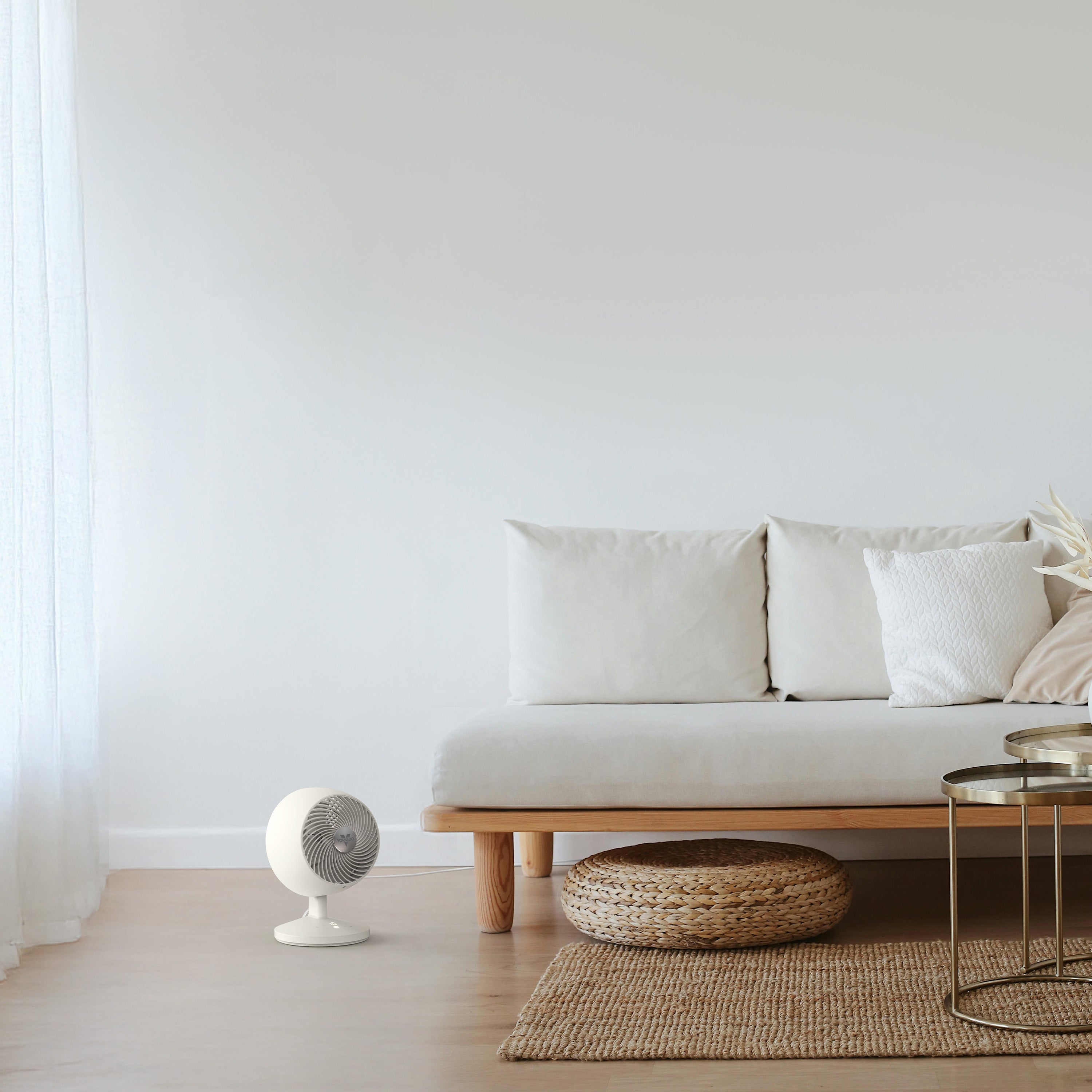 Modern living room with a white sofa, small fan, and decorative items.