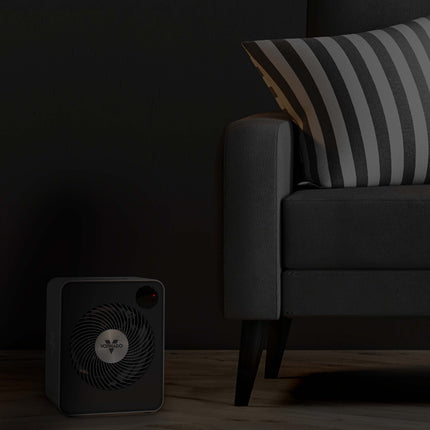 Small black heater on a wooden floor next to a gray sofa with striped cushions.