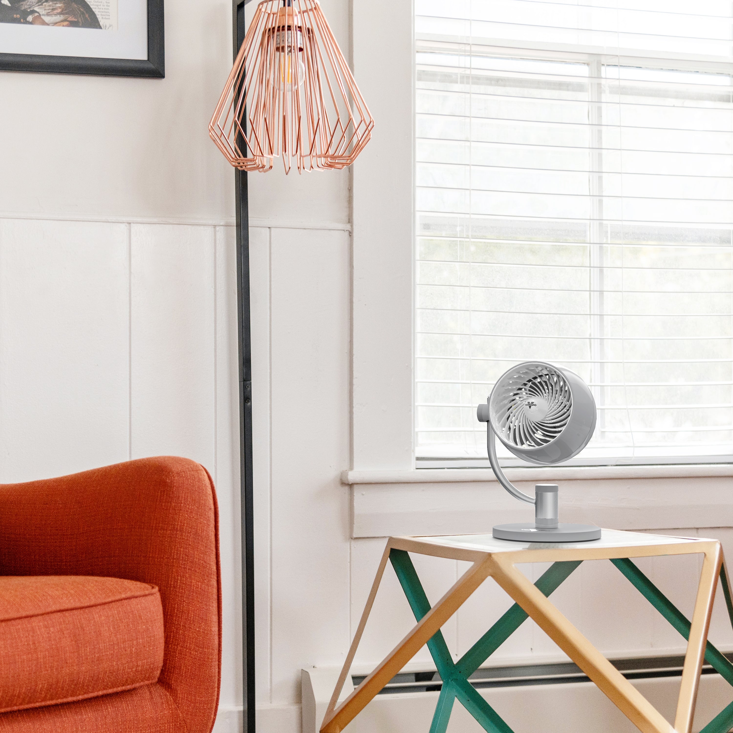 Modern living room with orange armchair, geometric table, and fan.