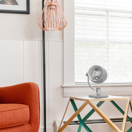 Modern living room with orange armchair, geometric table, and fan.