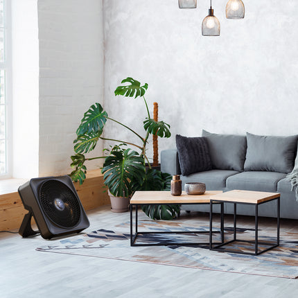 Modern living room with a gray sofa, coffee table, and box fan.