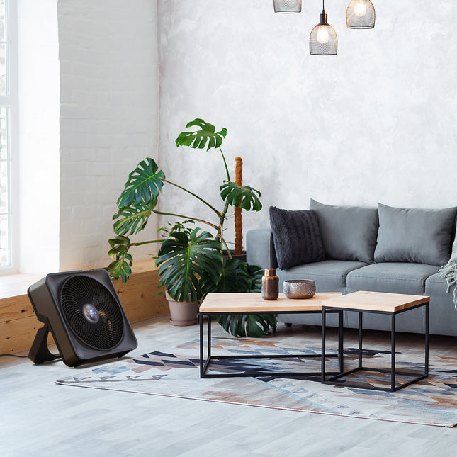 Modern living room with a gray sofa, coffee table, and box fan.