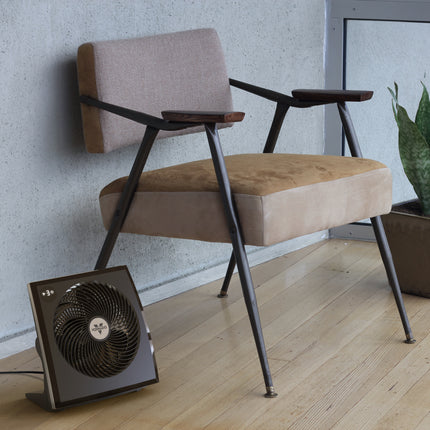 Modern chair with a plant and a small fan on a wooden floor.