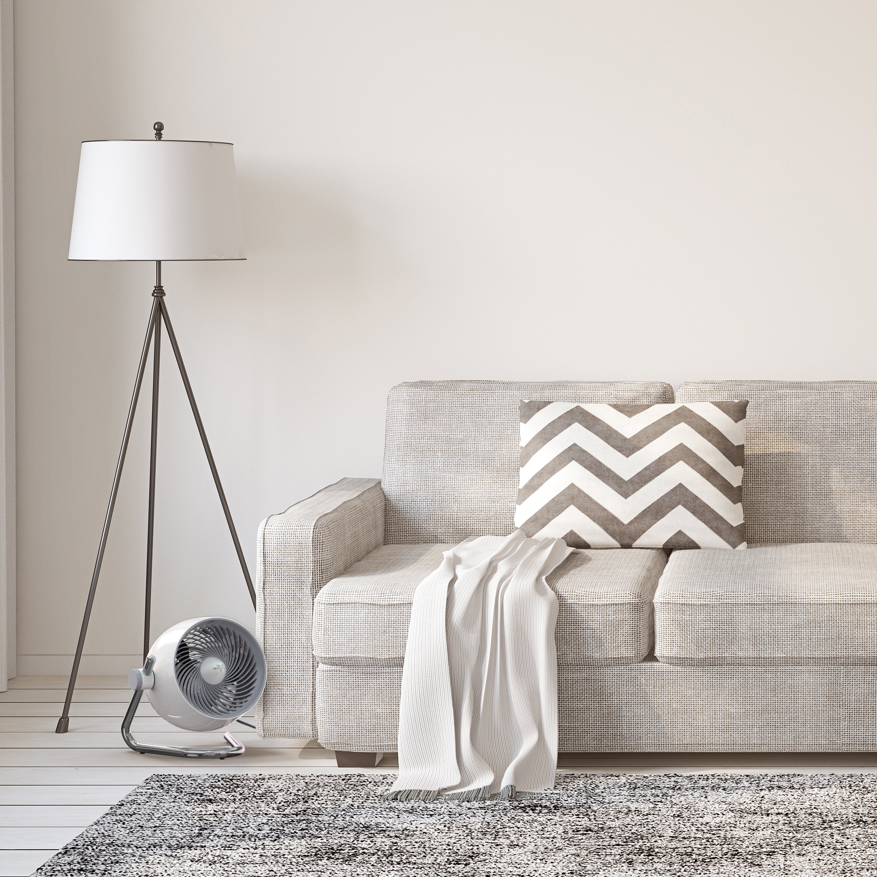 Gray sofa with a chevron-patterned pillow in a living room setting with a floor lamp and fan.