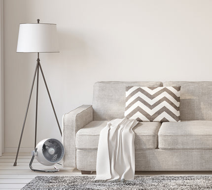 Gray sofa with a chevron-patterned pillow in a living room setting with a floor lamp and fan.