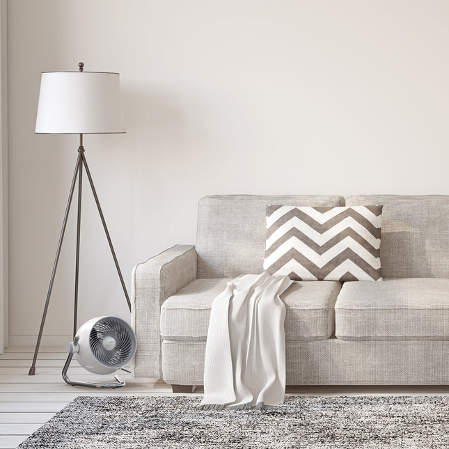 Gray sofa with a chevron-patterned pillow in a living room setting with a floor lamp and fan.