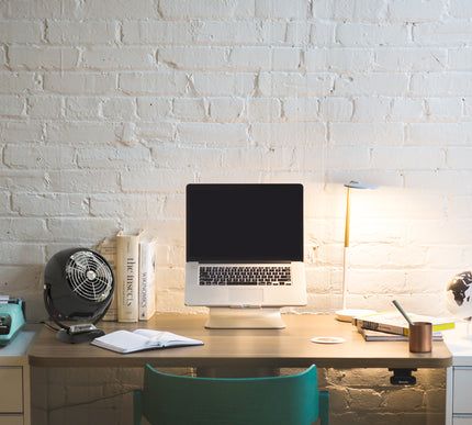 Home office desk with laptop, books, and lamp against a white brick wall.