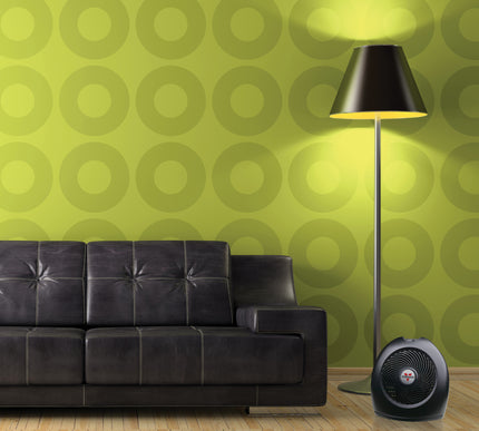 Black leather sofa in a room with green circular patterned wallpaper and a floor lamp.