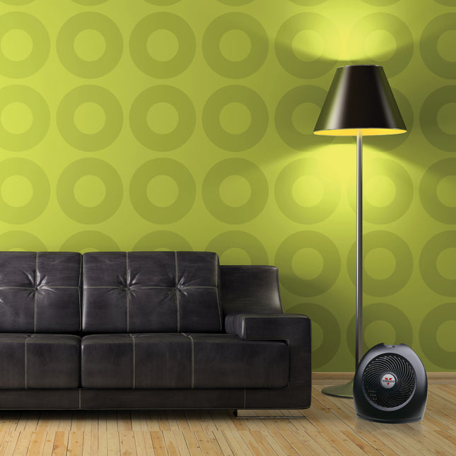 Black leather sofa in a room with green circular patterned wallpaper and a floor lamp.