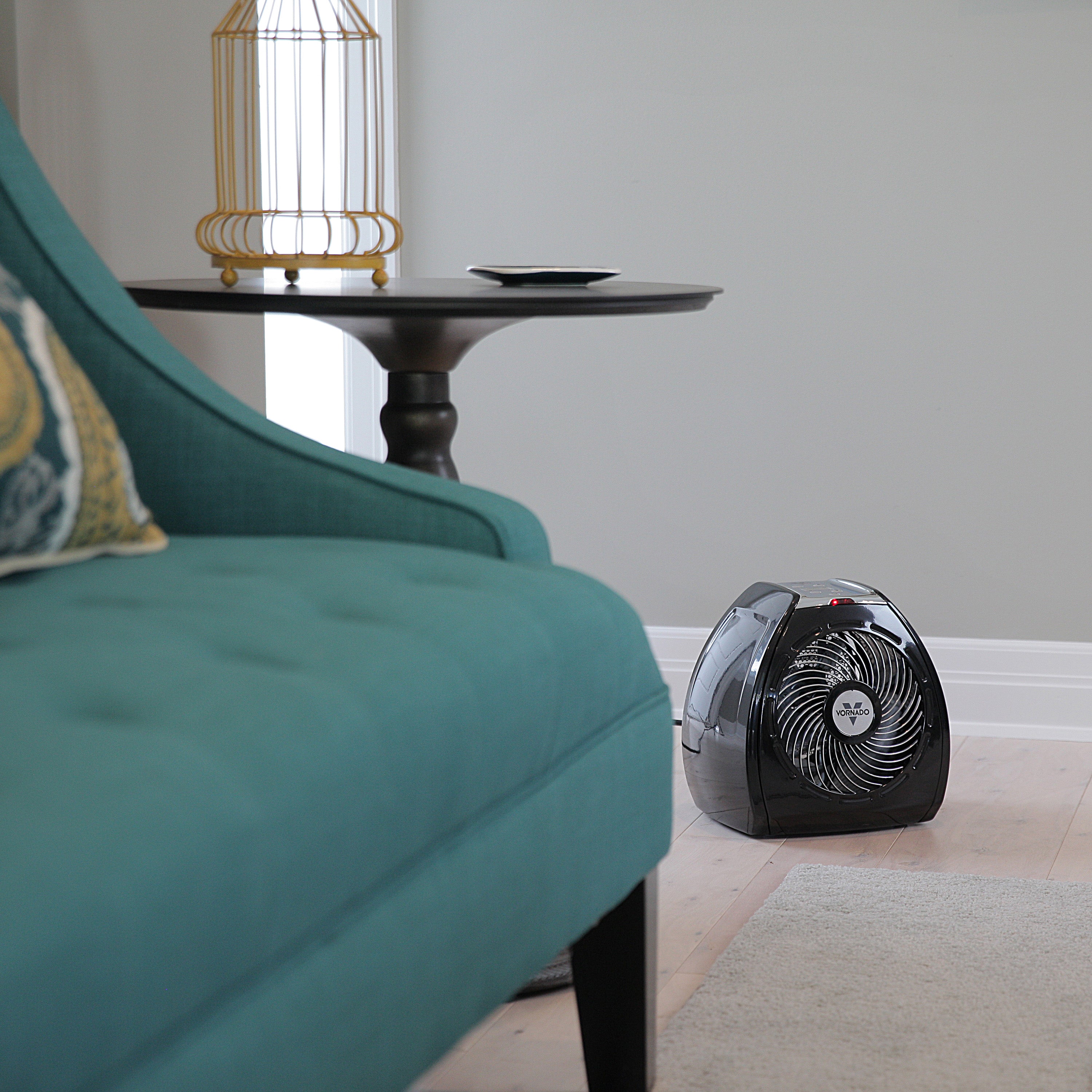 Small portable heater on a floor next to a teal sofa in a room with a side table and lamp.
