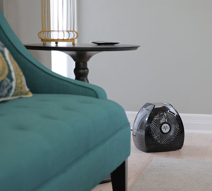 Small portable heater on a floor next to a teal sofa in a room with a side table and lamp.
