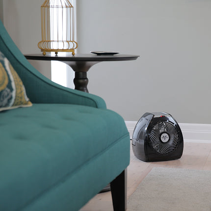 Small portable heater on a floor next to a teal sofa in a room with a side table and lamp.