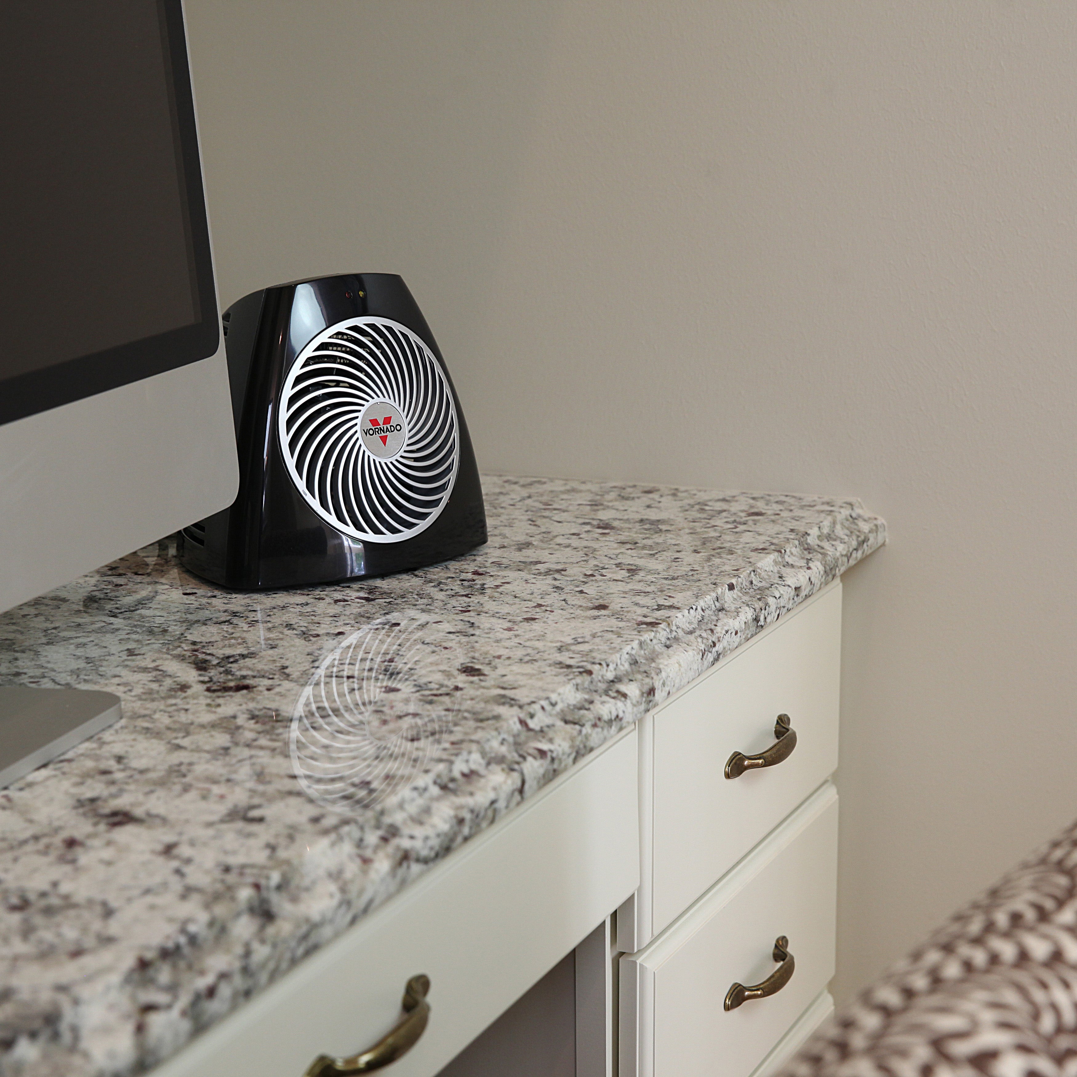 Black and white heater on a granite countertop next to a computer monitor.