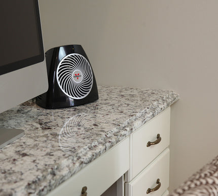 Black and white heater on a granite countertop next to a computer monitor.