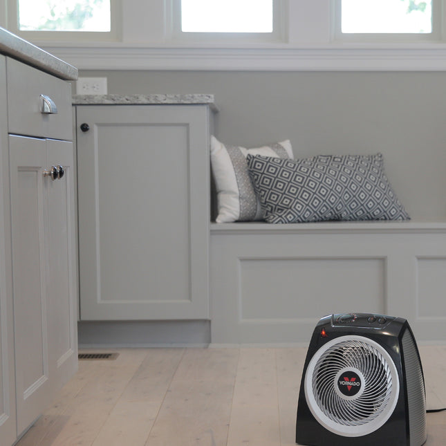 Black space heater on a tiled floor with a gray wall and window in the background