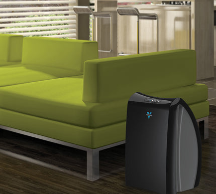 Black air purifier on a wooden floor next to a green sofa