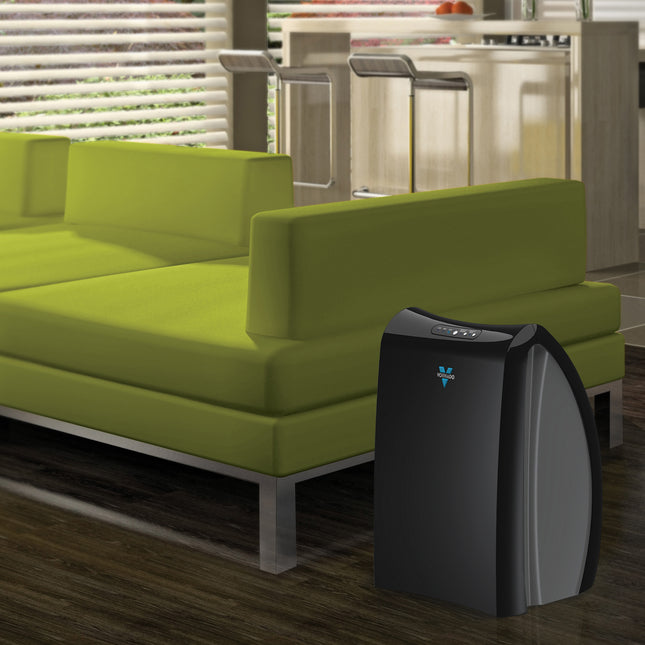 Black air purifier on a wooden floor next to a green sofa