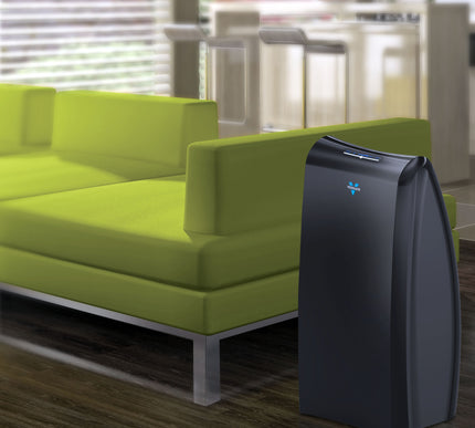 Air purifier next to a green sofa in a living room setting