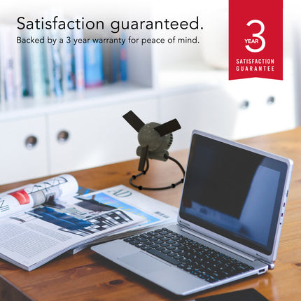 Laptop on a desk with a magazine and a 3-year satisfaction guarantee badge.