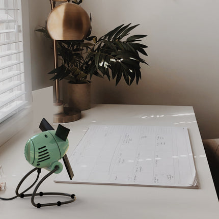 Small green fan on a desk with a calendar and plant in the background
