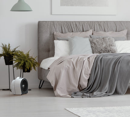 Modern bedroom with a bed, pillows, and a small heater on a light wooden floor.
