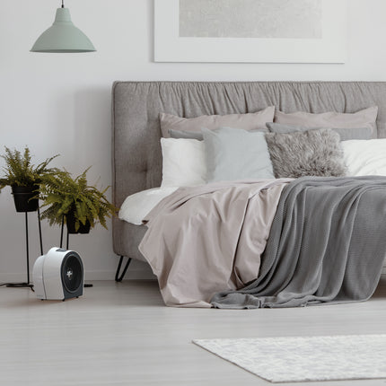 Modern bedroom with a bed, pillows, and a small heater on a light wooden floor.