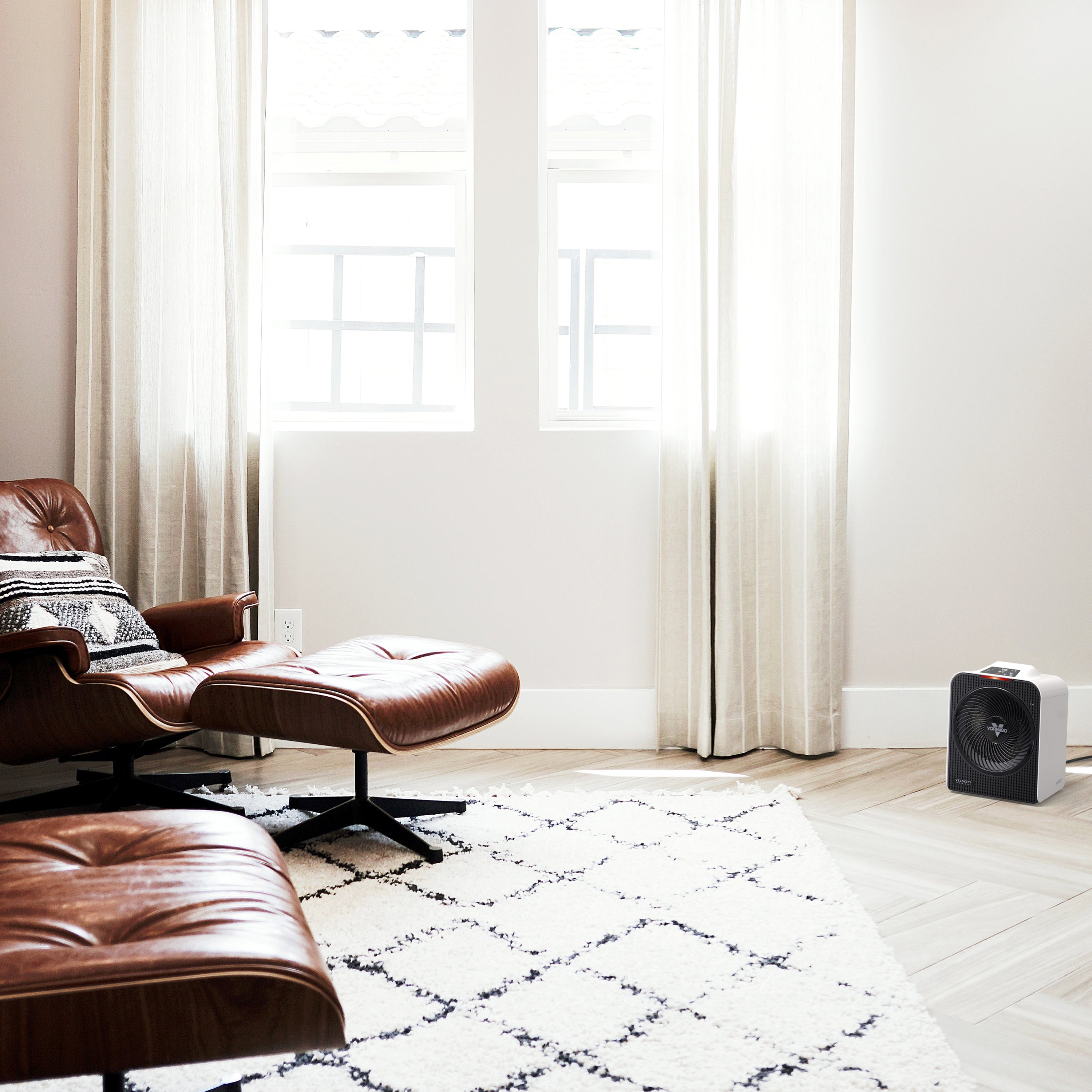 Modern living room with brown leather chair and ottoman, white walls, and large windows. White space heater on the floor.